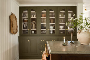 Green glass-front cabinet filled with dishes, glassware, and bowls in a bright kitchen.