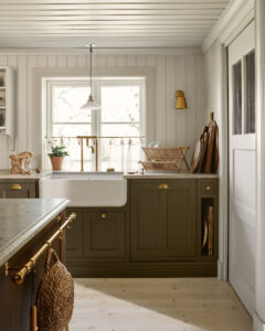 Light-filled cottage kitchen with gray cabinetry, white farmhouse sink under a window, and copper faucet under a pendant light.